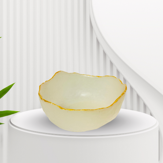 Oracryst selenite bowl with gold rim on a white pedestal against a white background with green leaves.